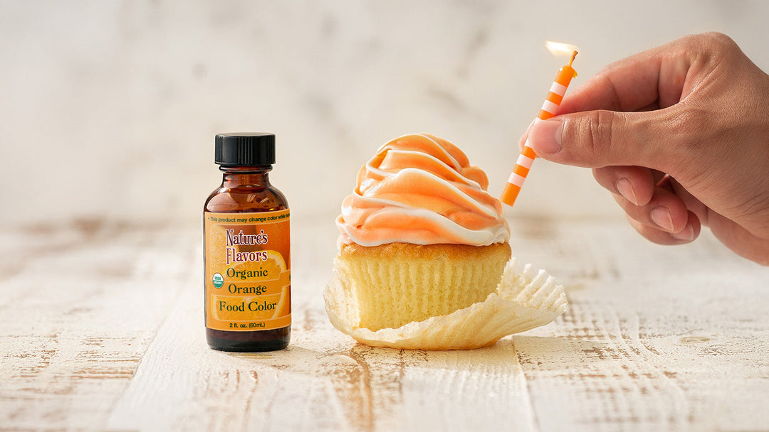 A hand placing a candle into a delicious cupcake with orange frosting using natures flavors natural orange food coloring