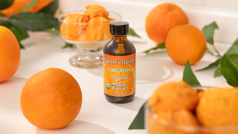 Orange Flavor Extract - Organic - bottle in the middle of actual oranges and a bowl of orange sherbet