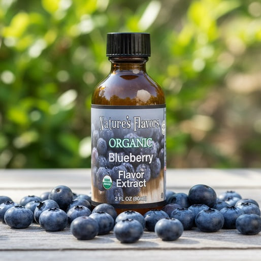 Bottle of Nature's Flavors Organic Blueberry Flavor Extract surrounded by blueberries on a wooden surface with a blurred green background.