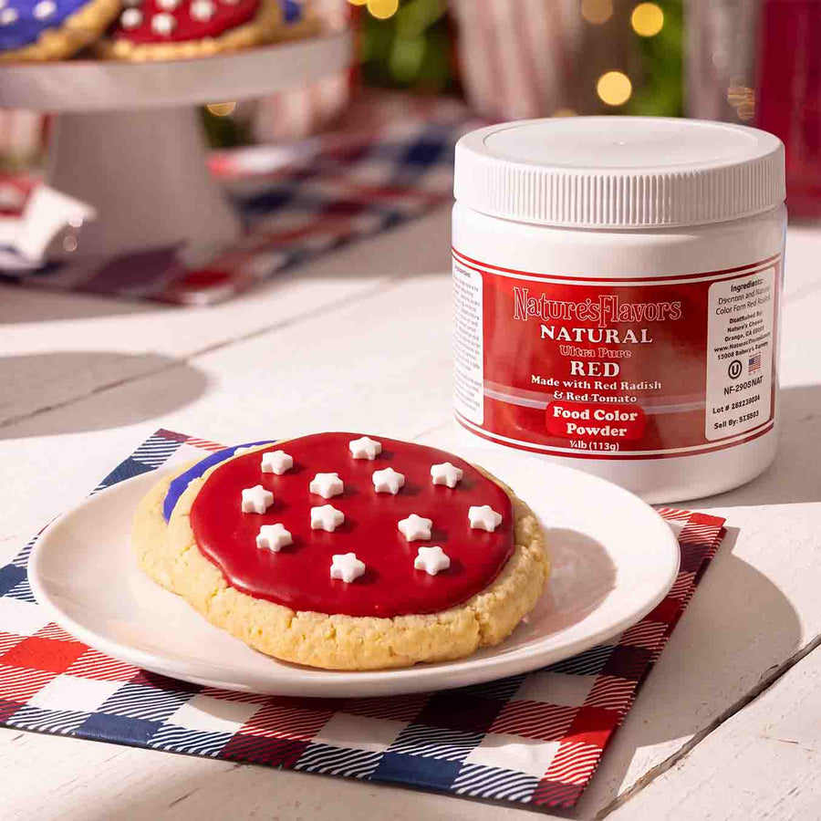White tub labeled, "Natural Ultra Pure Red Made with Red Radish & Red Tomato Food Color Powder" next to a plate with a red colored cookie on it. 