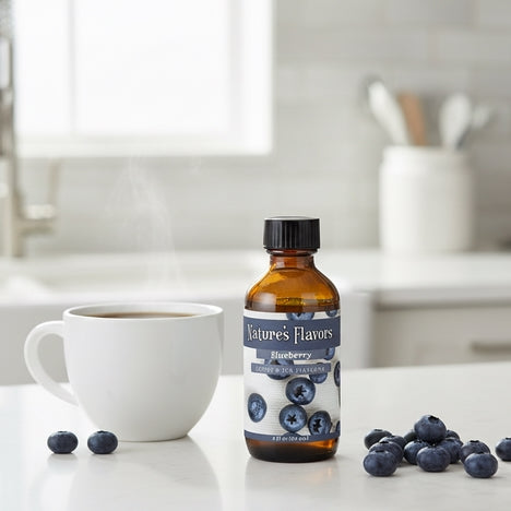 Bottle of Nature's Flavors Blueberry flavoring next to a cup of coffee and blueberries on a kitchen counter.