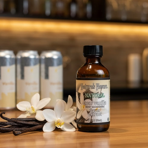 Bottle of Nature's Flavors Natural Clear Vanilla Flavor Extract with vanilla beans and flowers on a wooden surface.