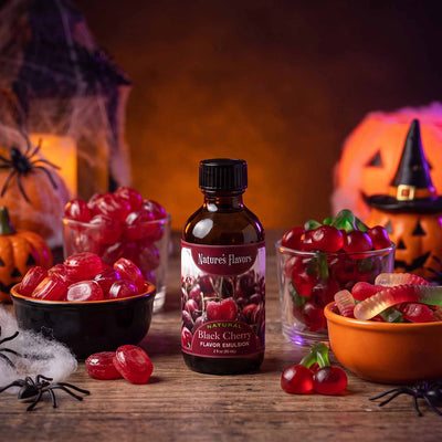Bottle Labeled, "Natural Black Cherry Flavor Emulsion" next to bowls of hard and gummy candy. 