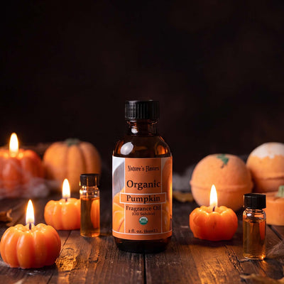 Bottle Labeled, "Organic Pumpkin Fragrance Oil (Oil Soluble) next to pumpkin themed candles and small bottles of perfume. 