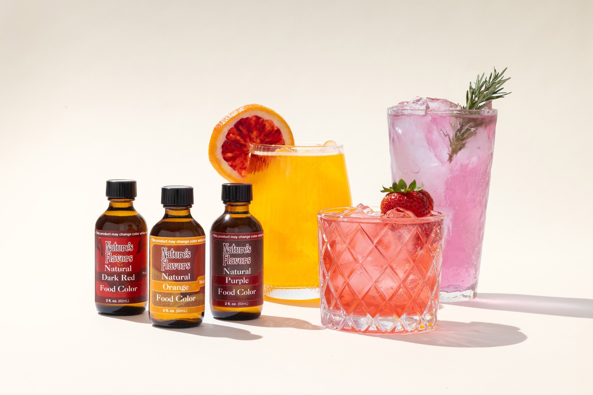 Three bottles of food coloring with colorful cocktails on a white background