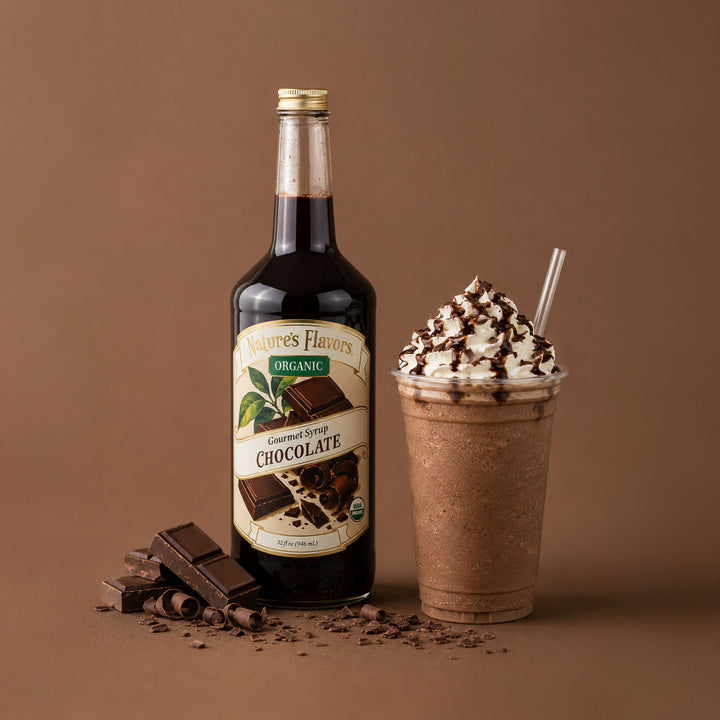 A bottle of Nature's Flavors Organic Chocolate Syrup stands next to a chocolate milkshake topped with whipped cream and drizzles, with chocolate pieces scattered on a brown studio background.