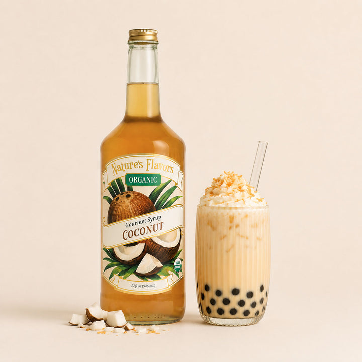 A bottle of Nature's Flavors Organic Coconut Syrup stands next to a glass of coconut boba milk tea with whipped cream and coconut flakes, on a warm beige background.