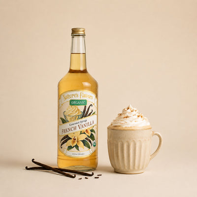 A bottle of Nature's Flavors Organic French Vanilla syrup stands next to a beige ceramic mug filled with whipped cream and a sprinkle of cinnamon, with vanilla beans on a warm beige background.