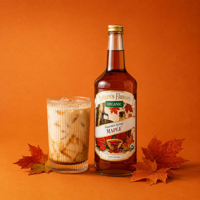A bottle of Nature's Flavors Organic Gourmet Syrup Maple stands next to a glass of iced maple latte on an orange background with autumn leaves.