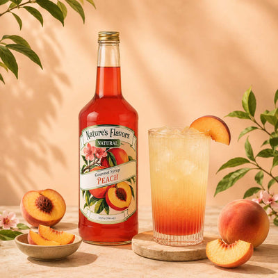 A bottle of Nature's Flavors Peach Syrup stands next to a tall glass of peach lemonade garnished with a peach slice, styled with fresh peaches and leaves on a warm beige background.