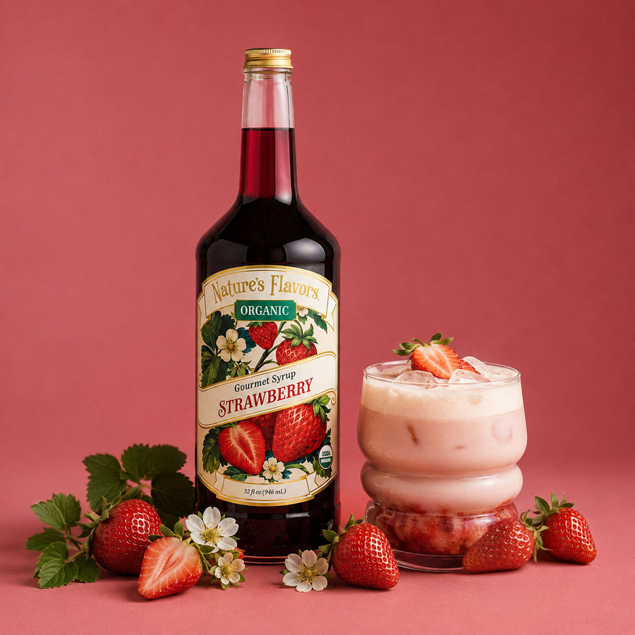 A bottle of Nature's Flavors Organic Strawberry Gourmet Syrup stands next to a pink strawberry drink in a glass, surrounded by fresh strawberries, strawberry leaves, and flowers on a solid pink background.