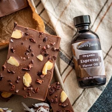 Chocolate bars with nuts and a bottle of Natures Flavors Organic Espresso Flavor Oil on a checkered fabric background.
