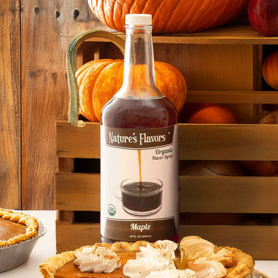 Bottle of Nature's Flavors maple flavored syrup with pumpkins and pies in the background
