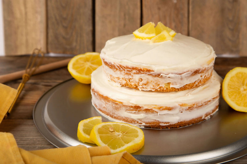 Two-layer lemon cake with white frosting on a wooden table with lemon slices.