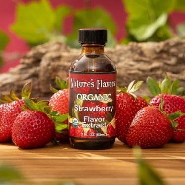 Bottle of Nature's Flavors Organic Strawberry Flavor Extract surrounded by strawberries on a wooden surface with a natural background.