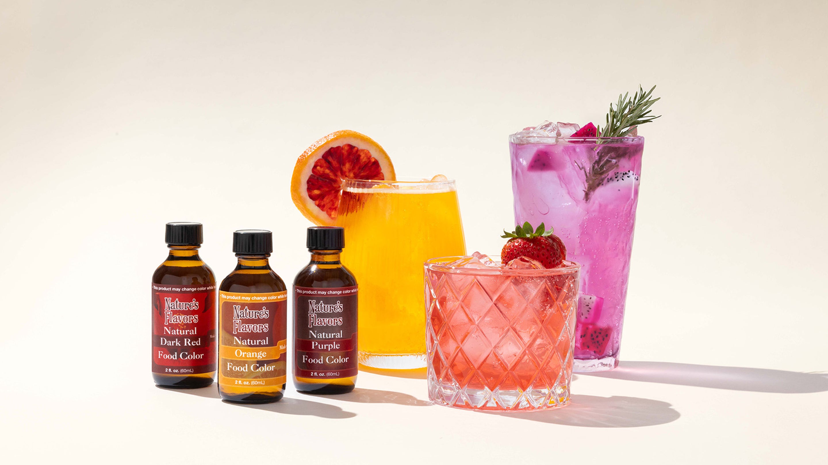 A selection of refreshing beverages colored with natural food coloring, including an orange cocktail, lavender spritz, and a sweet strawberry drink.
