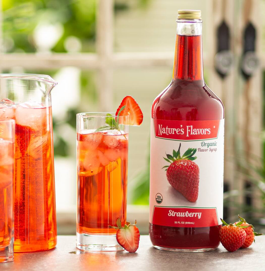 Nature's Flavors strawberry syrup bottle with glasses of strawberry-flavored iced tea outdoors.