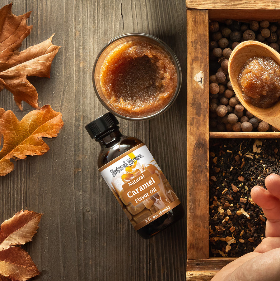 Bottle of Natural Caramel Flavor Oil on a wooden surface with autumn leaves and a wooden box of spices.