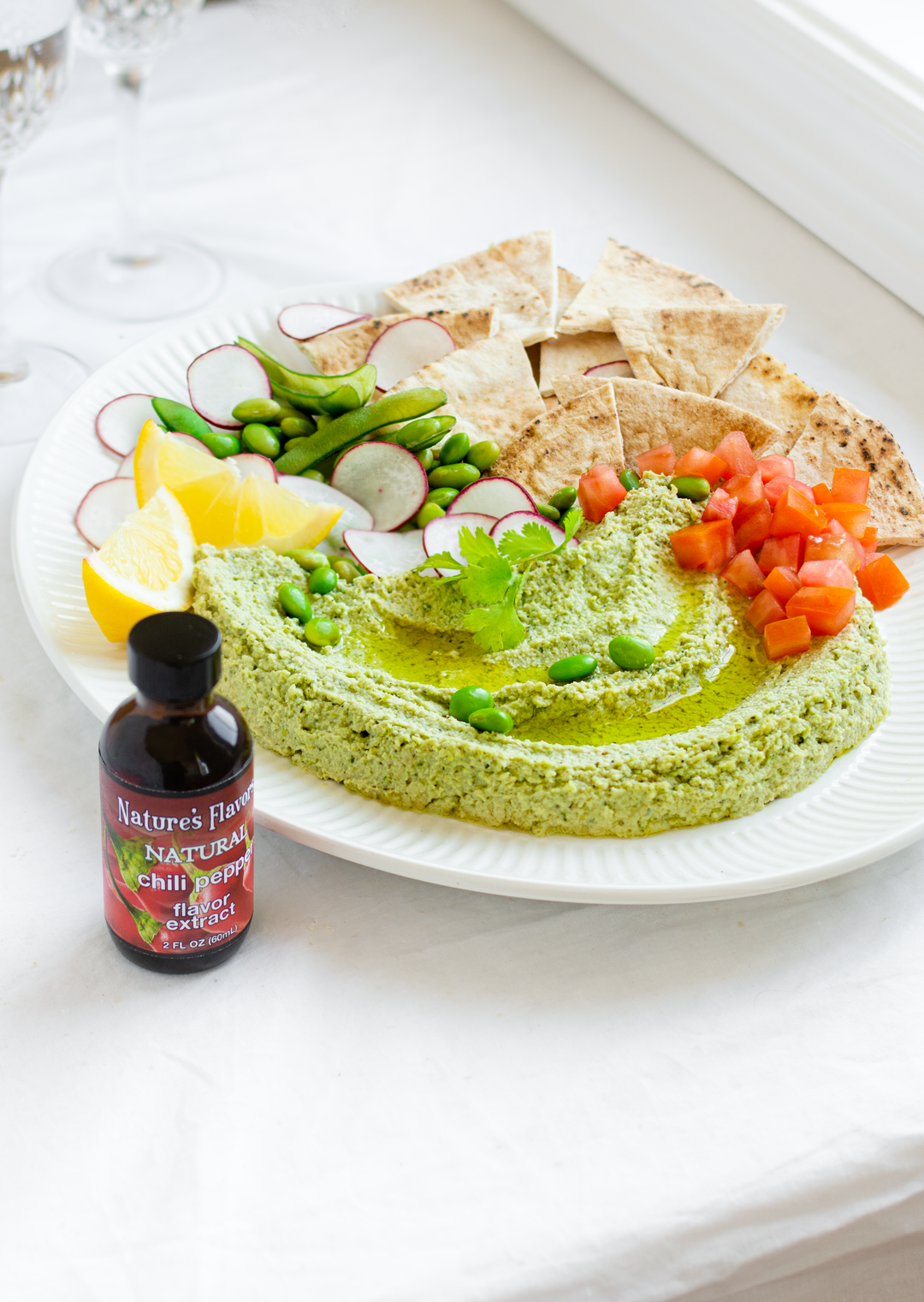 A tempting plate of hummus, pita and vegetables sits next to a bottle Nature's Flavors Natural Chili Pepper Flavor Extract, creating a warm and inviting atmosphere.