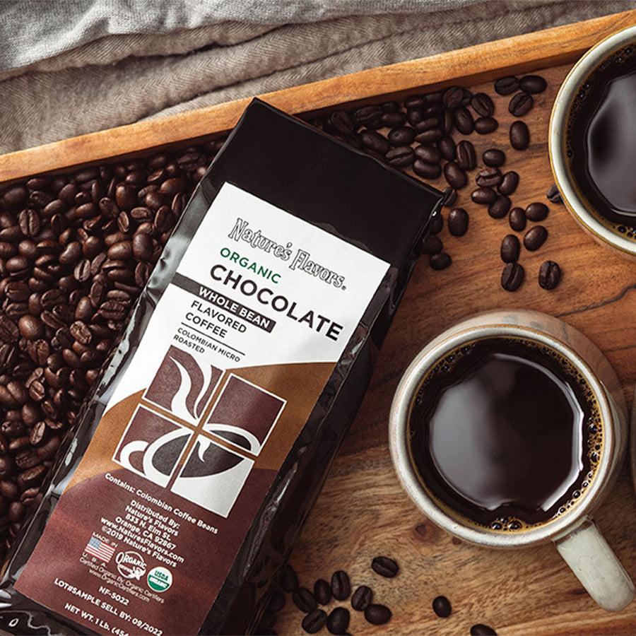 black bag labeled, "Organic Chocolate Flavored Coffee" on a bed of coffee beans next to a cup of coffee. 