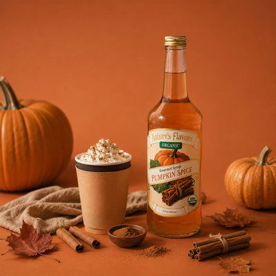 A bottle of Nature's Flavors Organic Pumpkin Spice syrup stands on a warm orange surface beside a pumpkin spice latte topped with whipped cream and cocoa, with pumpkins, cinnamon sticks, a small bowl of ground spice, and autumn leaves around it.