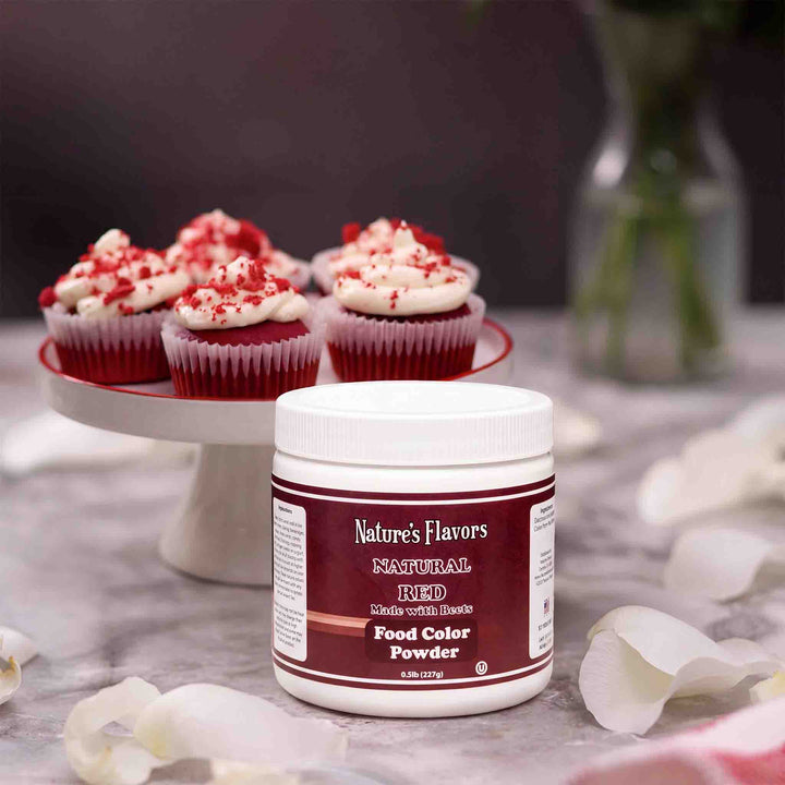Tub Labeled, "Natural Red Made With Beets Food Color Powder" with a plate of red cupcakes behind it. 