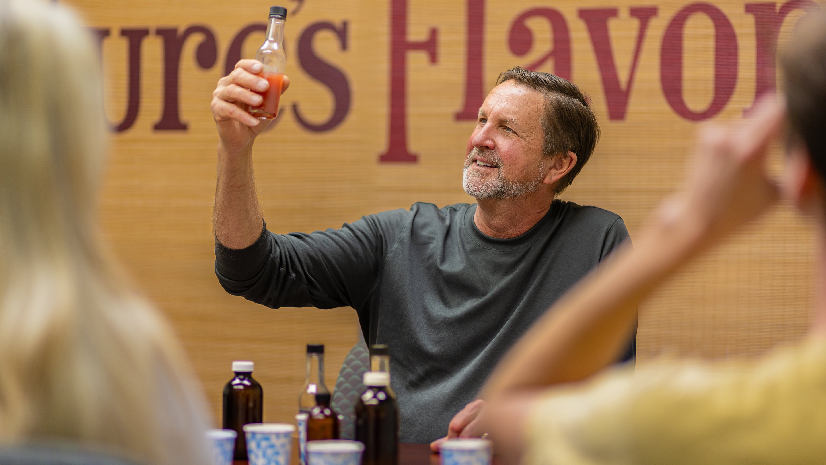 The Flavor Guy lifts a flavoring bottle up to the light to observe the color, while collaborating with two excited clients on a new product flavor development.