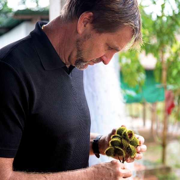 Man holding a small plant with greenery in the background