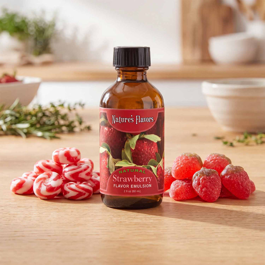 Bottle labeled, "Natural Strawberry Flavor Emulsion" surrounded by hard and gummy candies. 