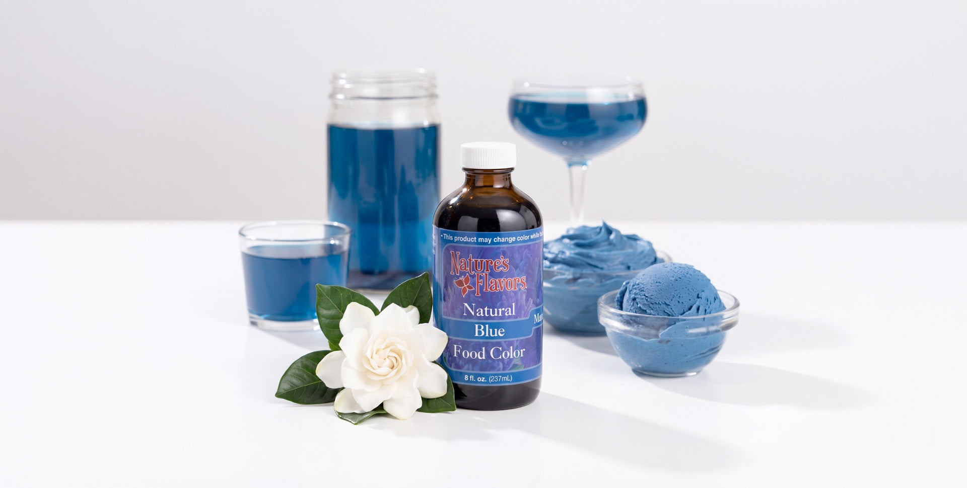 Blue-themed products including liquid, ice cream, frosting, on a white background. bottle of blue gardenia food coloring by nature's flavors in the center.