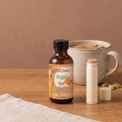 Natural Chai Flavor Oil for Lip Balm 2 oz bottle beside a large ceramic cup of chai, spices and an open lip balm tube.