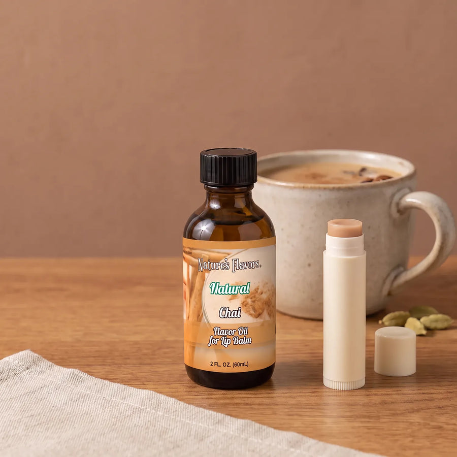 Natural Chai Flavor Oil for Lip Balm 2 oz bottle beside a large ceramic cup of chai, spices and an open lip balm tube.