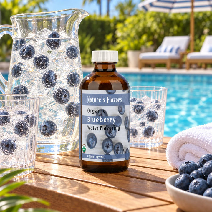 8 oz bottle of Nature's Flavors Organic Blueberry Water Flavoring by a pool beside a pitcher and glasses of sparkling water with blueberries