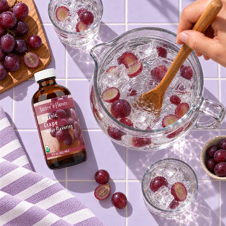 Overhead view of an 8 oz bottle of Nature's Flavors Organic Grape Water Flavoring on lavender tile beside a pitcher of water with grapes