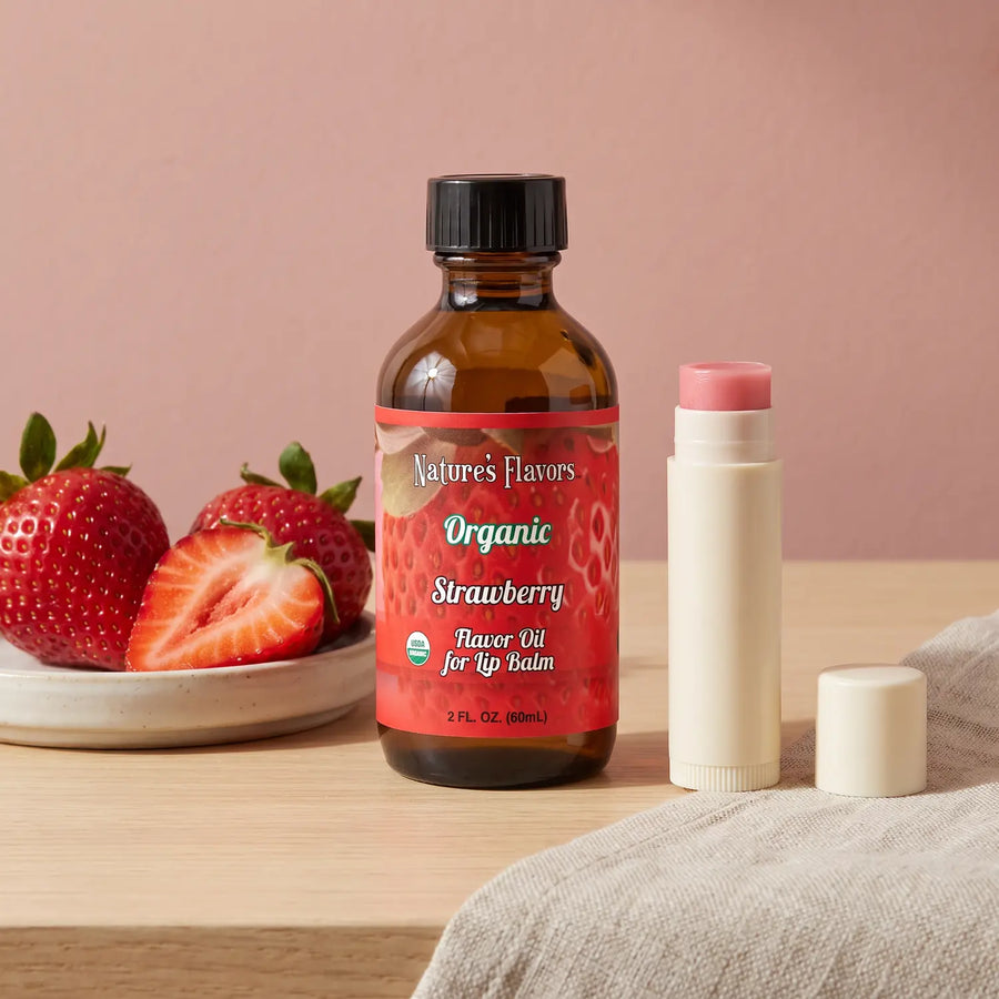 Nature's Flavors Organic Strawberry Flavor Oil for Lip Balm, 2 oz bottle with strawberries and an open unbranded lip balm tube.