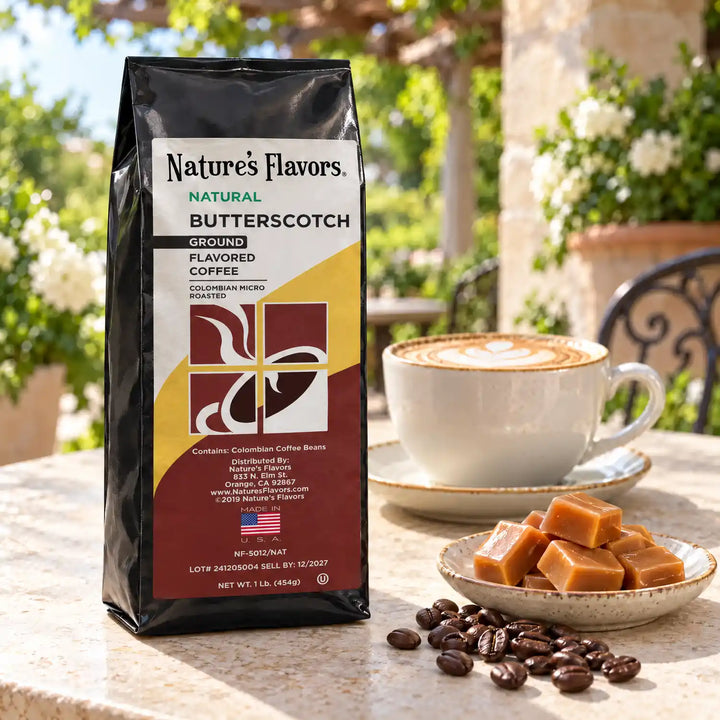 Nature’s Flavors Butterscotch Flavored Coffee Beans, 1 lb. Ground, in a black labeled bag beside butterscotch candies, whole roasted coffee beans and a filled coffee drink in a bright coffee scene.