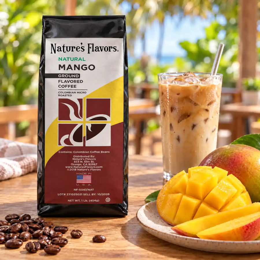 Nature’s Flavors Mango Flavored Coffee Beans, 1 lb. Ground, in a black labeled bag beside mango, whole roasted coffee beans and a filled coffee drink in a bright coffee scene.