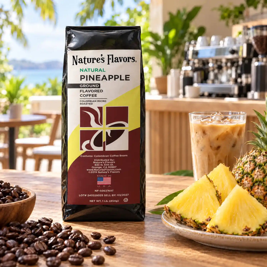 Nature’s Flavors Pineapple Flavored Coffee Beans, 1 lb. Ground, in a black labeled bag beside pineapple wedges, whole roasted coffee beans and a filled iced latte in a bright open-air tropical cafe.