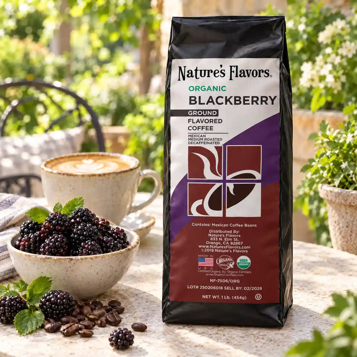 Nature’s Flavors Organic Decaf Blackberry Flavored Coffee Beans, 1 lb. Ground, in a black labeled bag beside blackberries, whole roasted coffee beans and a filled coffee drink in a bright coffee scene.