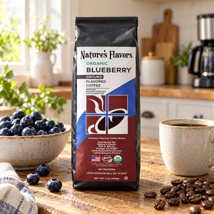 Nature’s Flavors Organic Decaf Blueberry Flavored Coffee Beans, 1 lb. Ground, in a black labeled bag with whole roasted coffee beans and a filled coffee drink in a bright farmhouse kitchen.