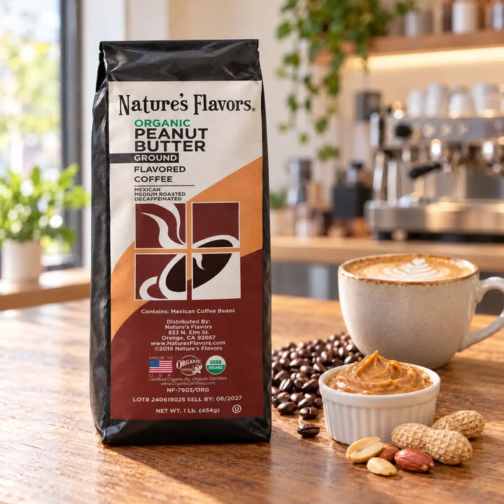 Nature’s Flavors Organic Decaf Peanut Butter Flavored Coffee Beans, 1 lb. Ground, in a black labeled bag beside peanut butter and peanuts, whole roasted coffee beans and a filled coffee drink in a bright coffee scene.