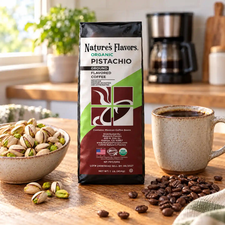 Nature’s Flavors Organic Decaf Pistachio Flavored Coffee Beans, 1 lb. Ground, beside a bowl of mostly split-shell pistachios, whole roasted coffee beans and a filled coffee mug in a bright rustic kitchen.