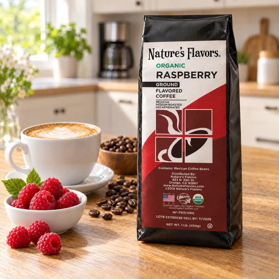 Nature’s Flavors Organic Decaf Raspberry Flavored Coffee Beans, 1 lb. Ground, in a black labeled bag beside raspberries, whole roasted coffee beans and a filled coffee drink in a bright coffee scene.