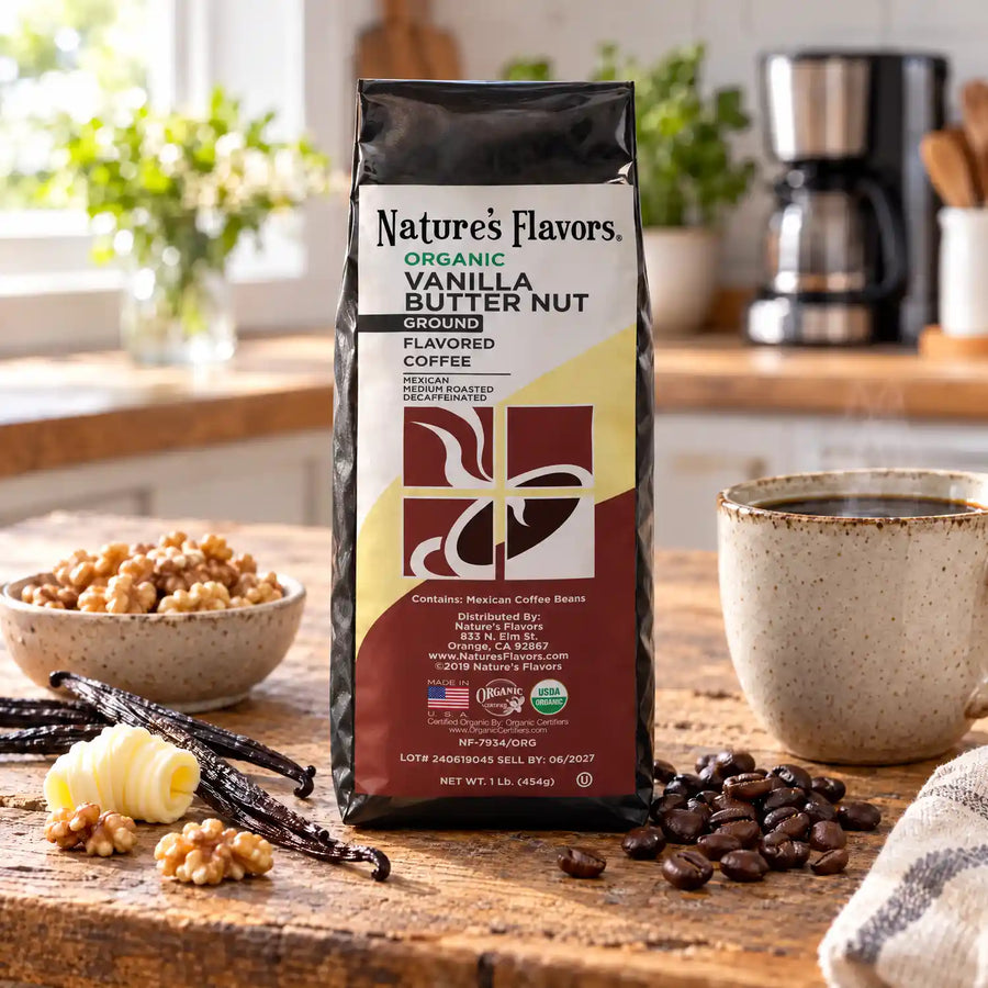 Nature’s Flavors Organic Decaf Vanilla Butter Nut Flavored Coffee Beans, 1 lb. Ground, in a black labeled bag with whole roasted coffee beans and a filled coffee drink in a bright rustic kitchen.