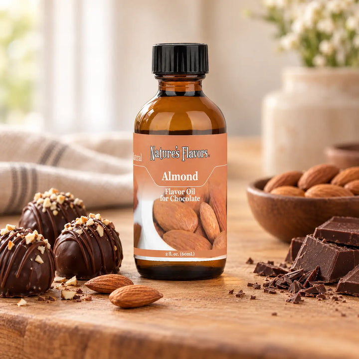 Nature's Flavors Almond Flavor Oil for Chocolate bottle on a wooden countertop beside chocolate truffles and almonds.