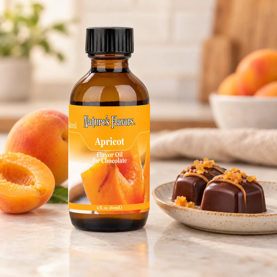 Nature's Flavors Apricot Flavor Oil for Chocolate bottle on a light countertop beside fresh apricots and chocolate bonbons.