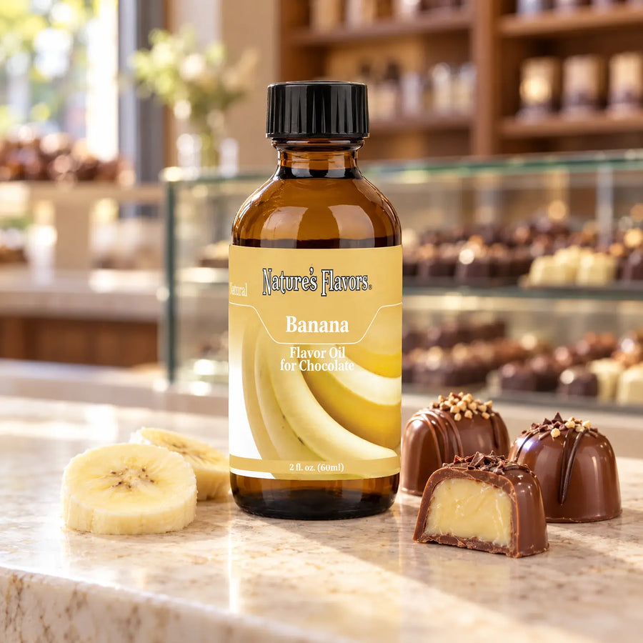 Nature's Flavors Banana Flavor Oil for Chocolate bottle beside banana slices and filled chocolate truffles on a chocolate-shop counter.