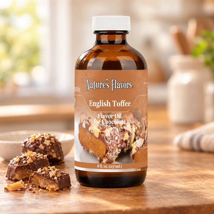 An eight-ounce bottle of Nature's Flavors English Toffee Flavor Oil for Chocolate with a white cap beside chocolate-covered toffee pieces.
