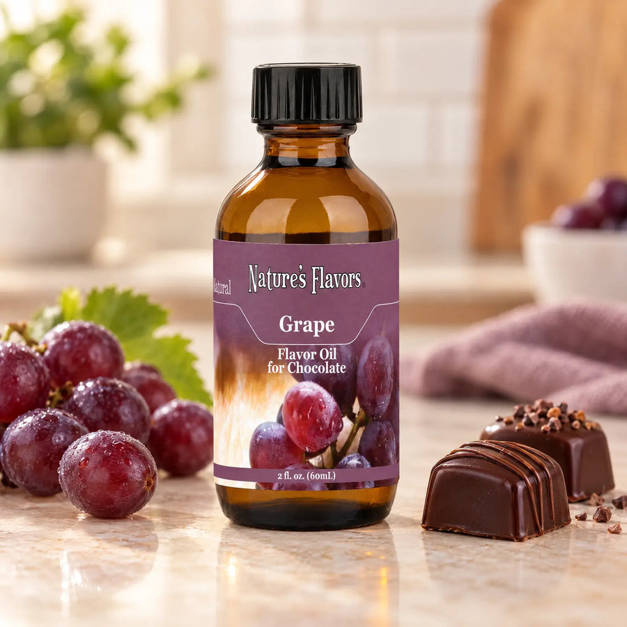 Nature's Flavors Grape Flavor Oil for Chocolate bottle beside purple grapes and dark chocolate bonbons on a light countertop.