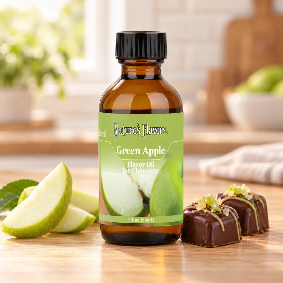 Nature's Flavors Green Apple Flavor Oil for Chocolate bottle beside green apple slices and chocolate bonbons on a wooden countertop.